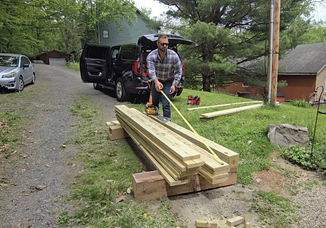 Matthew measuring pressure-treated framing lumber before a porch rebuild
